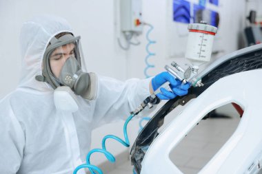 Kaportacıda sprey boyayla araba boyuyor.