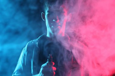 Koyu arkaplandaki neon ışıklarda elektronik sigara içen adam