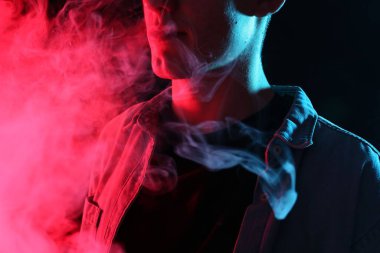 Siyah arka planda neon lambalarda elektronik sigara içen adam, yakın plan