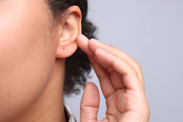 Young woman with pierced ear on light grey background, closeup