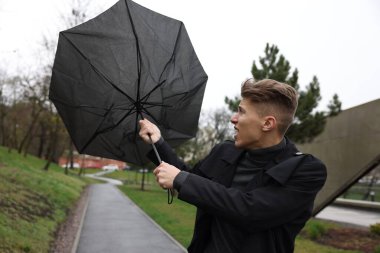 Kırık şemsiyeli bir adam açık havada yağmur altında rüzgarla savaşıyor.