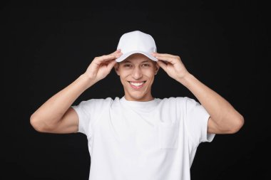 Siyah arka planda şık beyaz beysbol şapkası giyen genç bir adam.