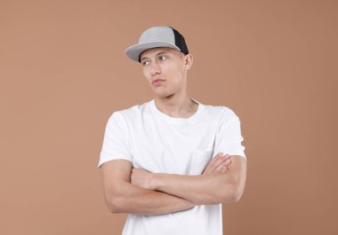 Açık kahverengi arka planda şık bir beyzbol şapkası giyen genç adam.