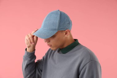 Pembe arka planda şık bir beyzbol şapkası takan genç adam.