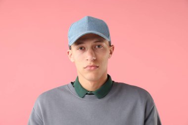 Pembe arka planda şık bir beyzbol şapkası takan genç adam.
