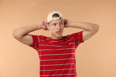 Beyzbol şapkalı genç adam bej arka planda.