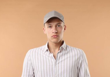 Beyzbol şapkalı genç adam bej arka planda.