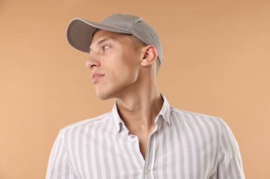 Beyzbol şapkalı genç adam bej arka planda.