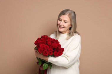 Bej arka planda bir buket gülle gülümseyen kadın.