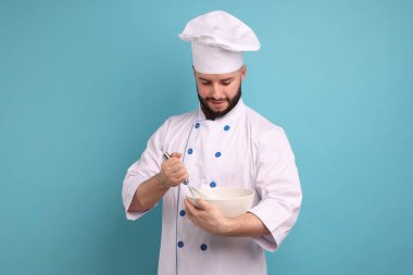 Üniformalı mutlu pastacı elinde çırpı ve kase ile açık mavi arka planda