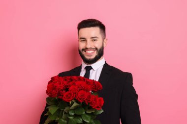 Pembe arka planda kırmızı güller açan mutlu bir adam.