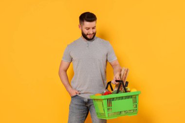 Turuncu arka planda ürünlerle dolu alışveriş sepeti olan bir adam.