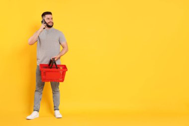 Boş alışveriş sepetli bir adam akıllı telefonuyla turuncu arka planda konuşuyor, mesaj için yer var.