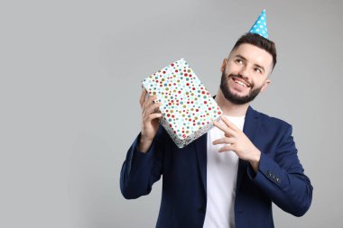 Doğum günün kutlu olsun. Gri arka planda parti şapkası ve hediye kutusu olan yakışıklı bir adam.