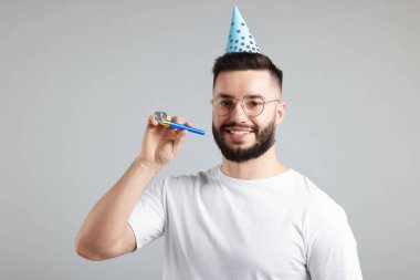 Doğum günün kutlu olsun. Gri arka planda parti şapkası ve üflemeli yakışıklı bir adam.