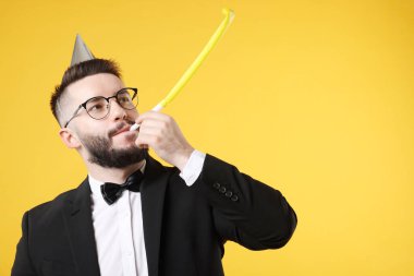 Doğum günün kutlu olsun. Turuncu arka planda parti şapkası ve üfleyicisi olan yakışıklı bir adam.