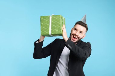 Doğum günün kutlu olsun. Açık mavi arka planda parti şapkası ve hediye kutusu olan yakışıklı bir adam.