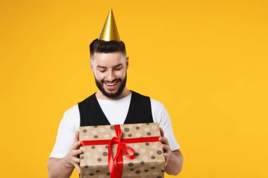 Doğum günün kutlu olsun. Turuncu arka planda parti şapkası ve hediye kutusu olan yakışıklı bir adam.