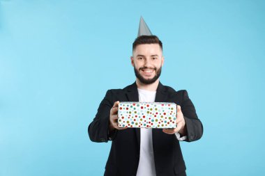 Doğum günün kutlu olsun. Açık mavi arka planda parti şapkası ve hediye kutusu olan yakışıklı bir adam.