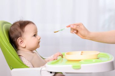 Anne bebeğini sandalyeyle besliyor, yakın plan.