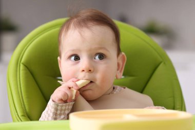Evdeki beslenme sandalyesinde yemek yiyen şirin bir bebek.