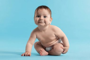 Açık mavi arka planda oturan, bebek bezi takmış şirin bir bebek.