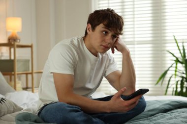 Gençlik sorunları. Evde akıllı telefonlu üzgün bir genç çocuk.
