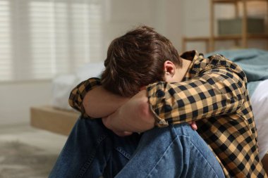 Gençlik sorunları. Evde yatağın yanında depresyonda olan genç bir çocuk.