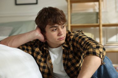 Gençlik sorunları. Evde yatağın yanında üzgün bir genç çocuk var.