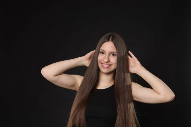 Siyah arka planda sağlıklı uzun saçlı, gülümseyen genç kızın portresi.