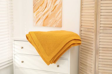 İçerideki beyaz çekmecelerin üzerine turuncu yün battaniye.