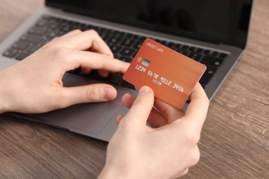 Çevrimiçi ödeme. Kredi kartlı bir kadın, ahşap masada dizüstü bilgisayarda yazı yazıyor.