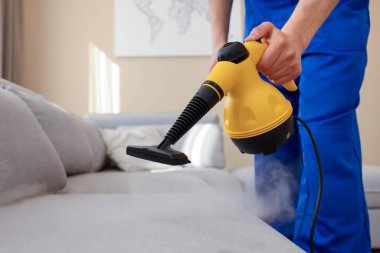 Temizlikçi kanepeyi evde buharlı temizleme makinesiyle temizliyor.