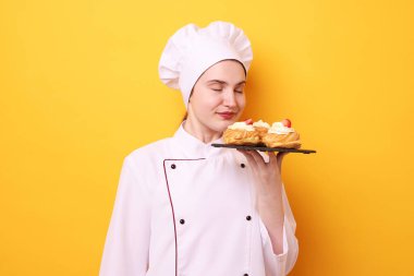 Üniformalı şekerci turuncu arka planda lezzetli profiteroller tutuyor.