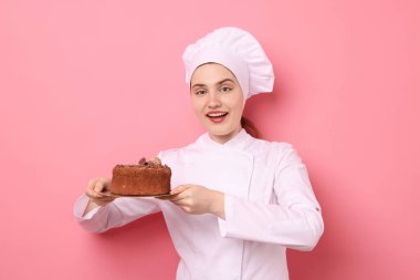 Üniformalı pastacı pembe arka planda lezzetli çikolatalı pasta tutuyor.