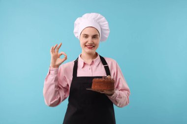 Lezzetli çikolatalı pastalı pastacı açık mavi arka planda iyi bir jest gösteriyor.