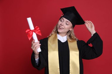 Mezun olduktan sonra kırmızı arka planda diplomalı mutlu bir öğrenci.