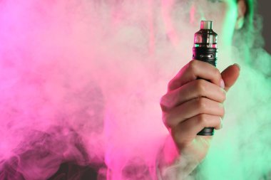 Gri arka planda neon lambalarda elektronik sigara içen kadın, yakın plan