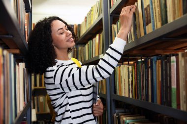 Bilgisayarlı bir kadın kütüphanedeki raftan kitap seçiyor.