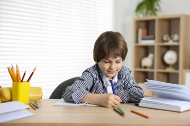 Evde, masada ödev yapan sevimli küçük çocuk.