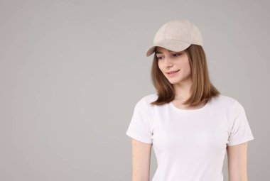 Açık gri arka planda şık bej beysbol şapkası takan genç bir kadın.