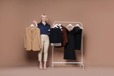 Gülümseyen moda tasarımcısı ve bej arka planda giysileri olan askılar.