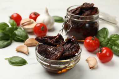 Lezzetli güneşte kurutulmuş domatesler, taze sebzeler, fesleğen ve sarımsak beyaz masada, yakın plan.