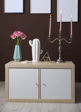 Kahverengi duvarın yanındaki dolapta yanan mumlar ve dekorlar olan zarif bir şamdan.