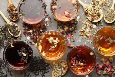 Cam fincanlarda aromatik bitki çayı, kuru yapraklar ve gri masada çiçekler, düz uzanmış