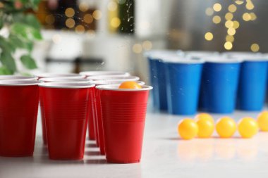 Aydınlık masada, bulanık ışıklara karşı plastik bardağa düşen turuncu top. Bira pong oyunu