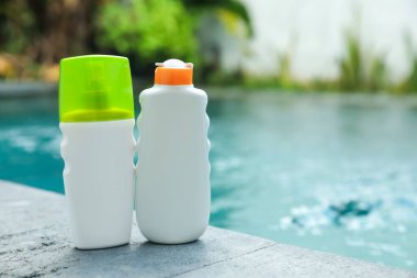 Dışarıdaki yüzme havuzunun yakınındaki taş yüzeyde güneş koruma ürünleri şişeleri, metin için yer.