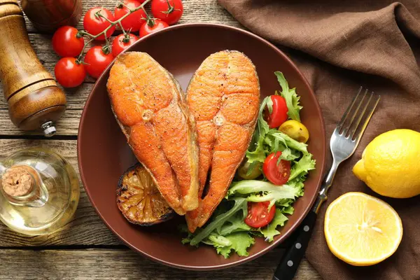 Deniz ürünleri. Tahta masada salata ve limonla servis edilen lezzetli somon biftekleri.