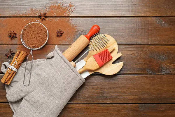 Farklı mutfak aletleri fırın eldivenlerinde, kakao tozu, tarçın ve anason yıldızları tahta masada, düz yerde