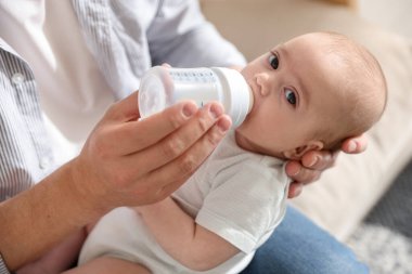 Babası evdeki kanepede bebeğini biberonla besliyor.